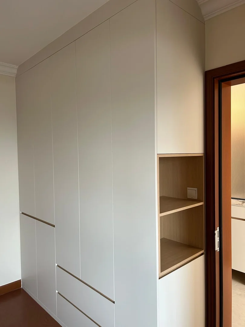 Full-height white HDB wardrobe with wood-look side open shelves beside a bedroom doorway