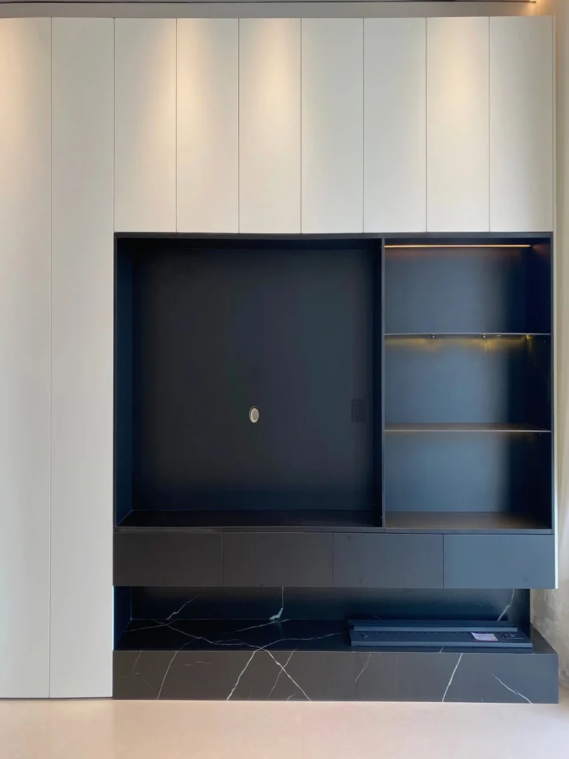 Full-height white TV wall storage with a black TV niche, illuminated display shelves and dark floating console in a Singapore HDB living room